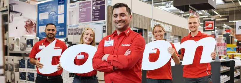 Fünf Toom Mitarbeiter in roter Arbeitskleidung halten die Buchstaben T O O M hoch